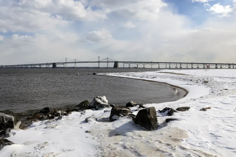 The Chesapeake Bay Bridge stretching across the bay, seen from a snowy beach at Sandy Point