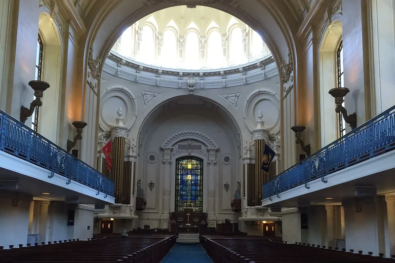 The interior of the Naval Academy Chapel with pews, a blue carpet aisle and the dome above