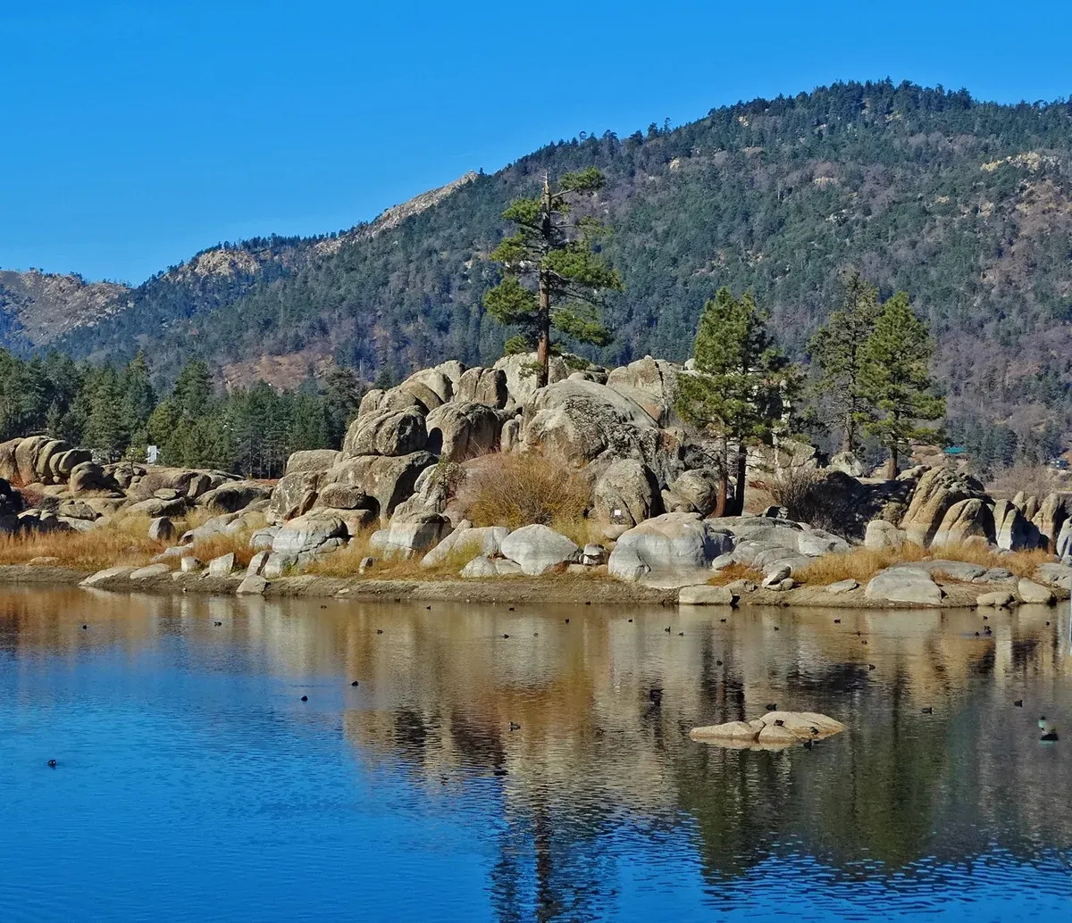 Granite boulders and pines on the shore of Boulder Bay, Big Bear Lake, with calm blue water and wooded hills