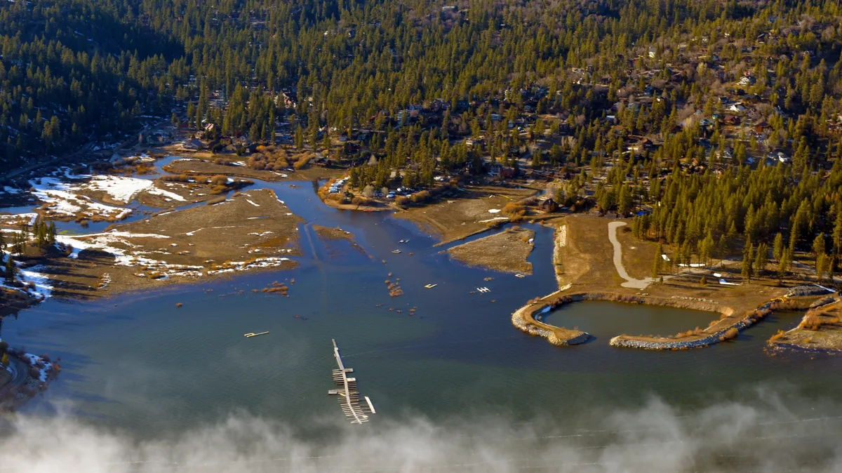 An aerial view of the east end of Big Bear Lake with low cloud, shoreline and pine-covered slopes