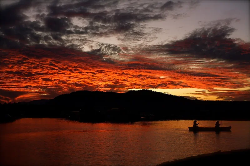 A deep orange and red sunset over Big Bear Lake with a small boat silhouetted on the water