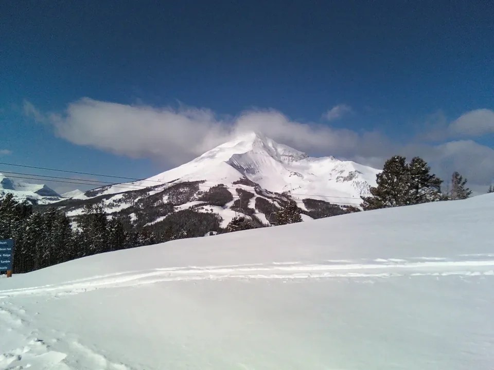 The snowy pyramid of Lone Peak above forested ridges at Big Sky, seen from a smaller mountain across the valley