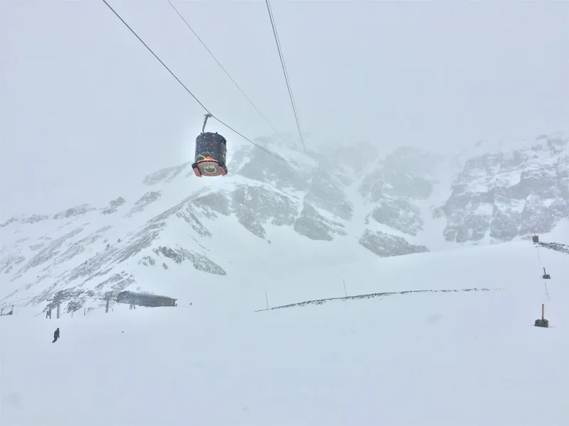 The Lone Peak Tram car hanging on its cables above the snowy upper slopes of Lone Peak in flat January light