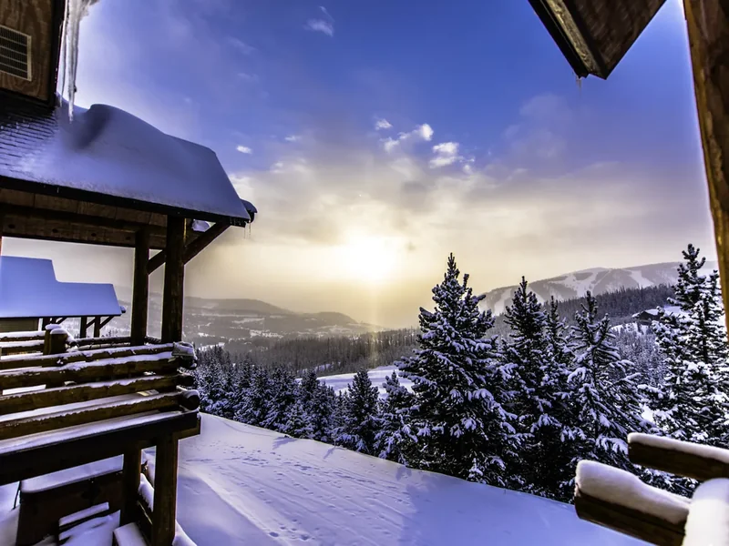 Sunrise light over snowy hills seen from a snow-covered wooden deck and railing in Big Sky