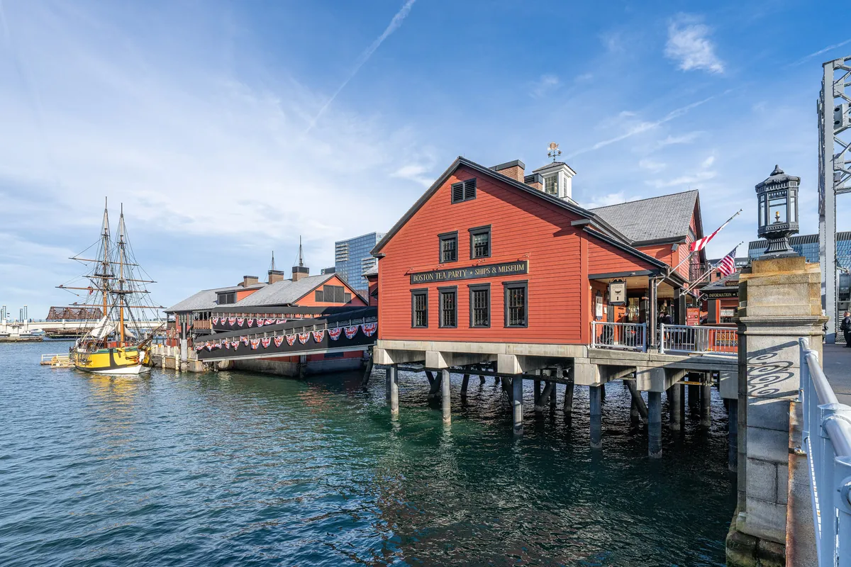 The red Boston Tea Party museum building on a pier over the Fort Point Channel, with a replica tall ship moored beside it