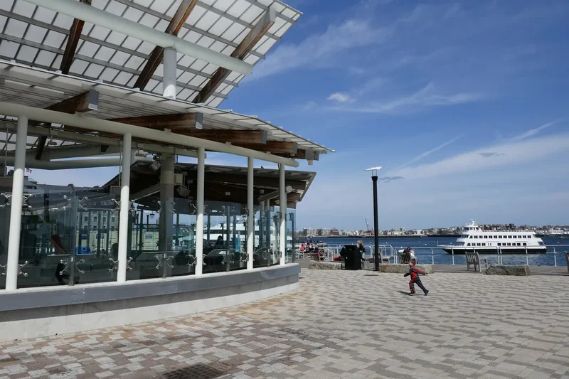 The glass-fronted New England Aquarium on Central Wharf beside the Boston Harborwalk, with the harbor behind