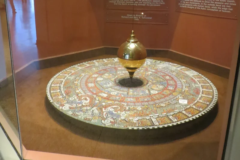 A Foucault pendulum swinging over a round dial at the Museum of Science in Boston