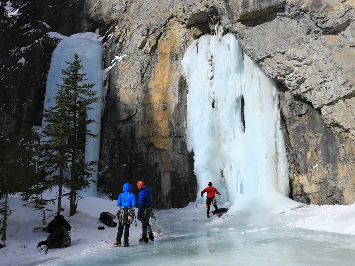 Walkers on the frozen floor of Grotto Canyon below a tall frozen waterfall of blue ice