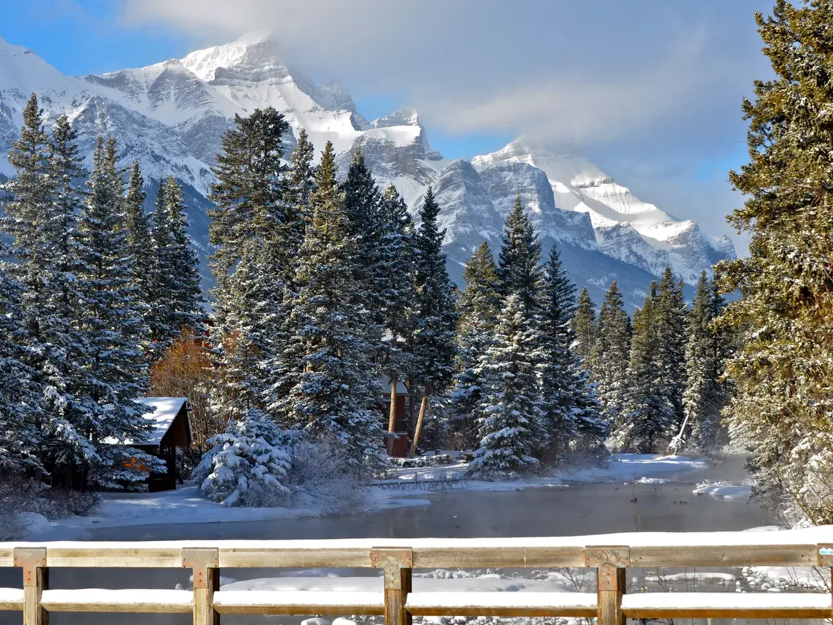 The Policeman Creek boardwalk in Canmore under snow, with frosted spruce trees and jagged snowy peaks behind