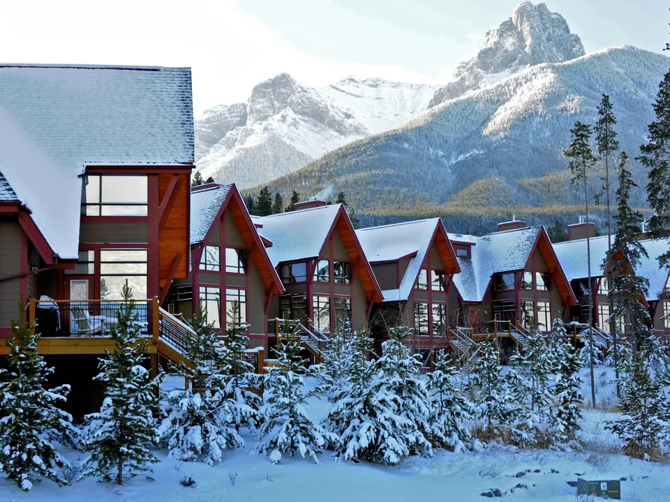 Red-roofed wooden chalets in Canmore under fresh snow, with snowy spruce and a peak behind