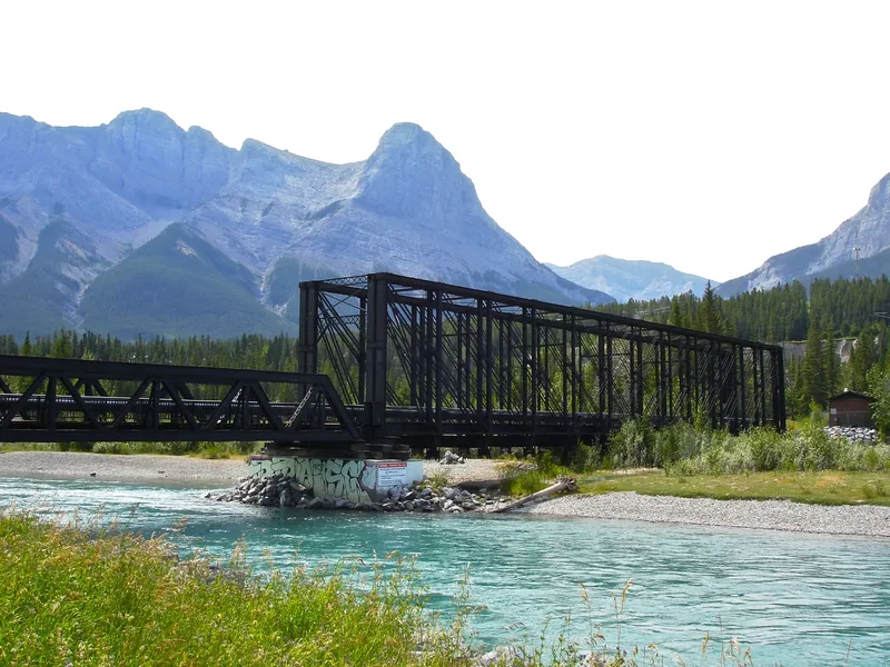 The black iron Engine Bridge crossing the turquoise Bow River in Canmore, with a peak behind