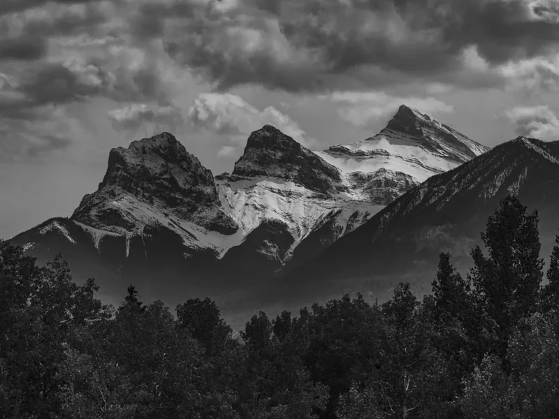 A black-and-white view of the jagged Three Sisters peaks above a dark forest