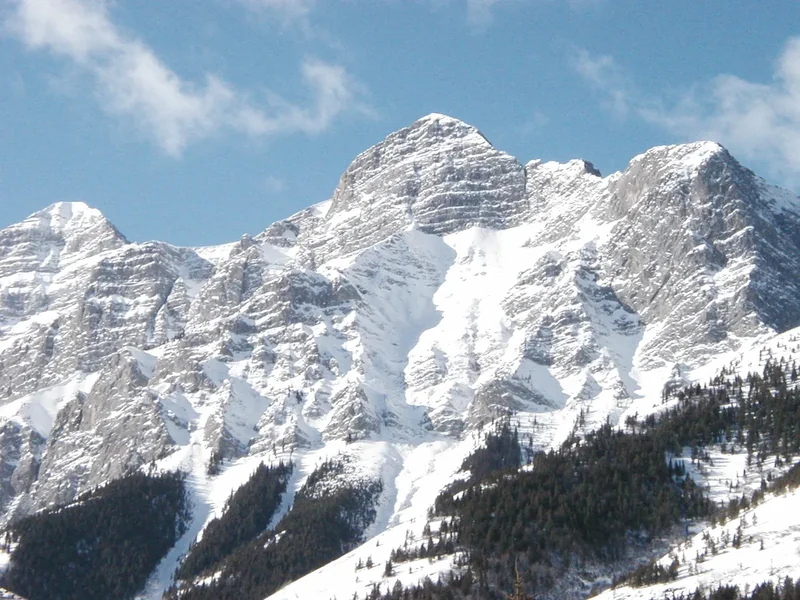 A snowy, rocky mountain face rising above Kananaskis Village under a pale blue sky