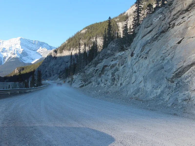 A snowy mountain road near Canmore curving below a pale cliff and a snow-covered peak