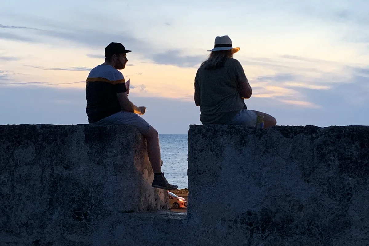 Two people sitting on the old city walls at sunset, seen in silhouette