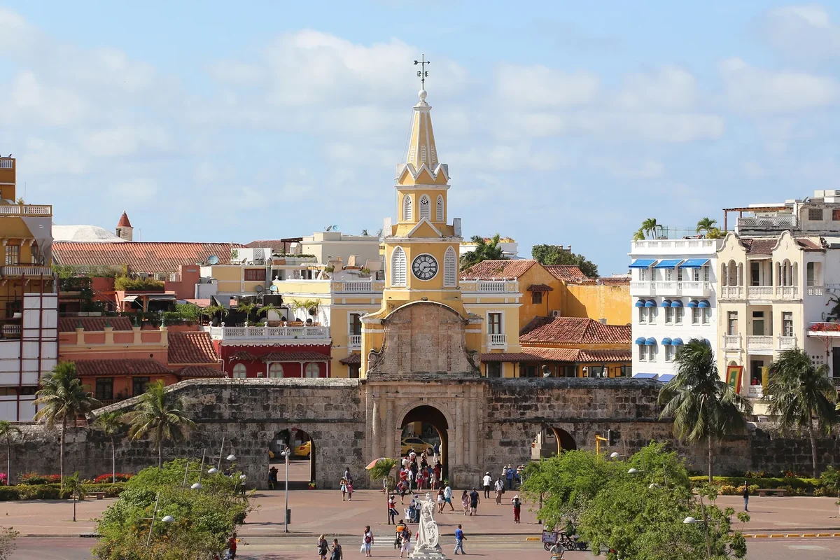 The Puerta del Reloj clock tower gate in Cartagena under a blue sky, with palms and the plaza in front