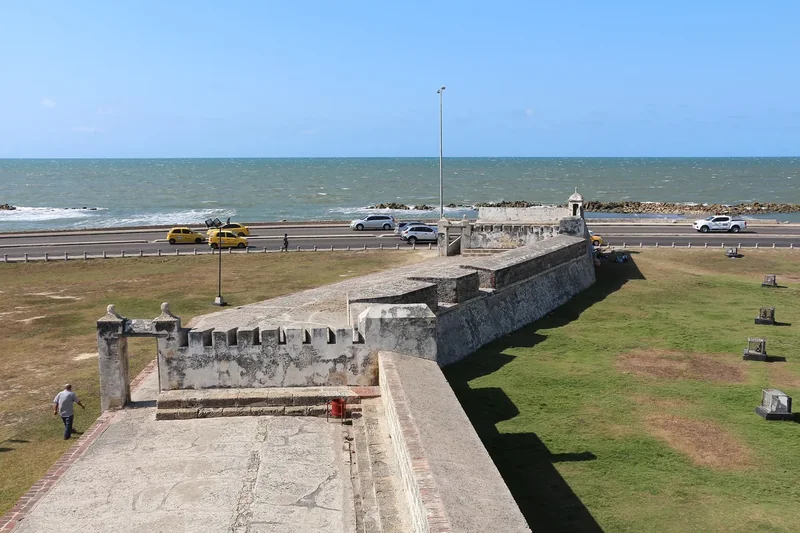 A section of the old city walls between a grassy moat and the sea