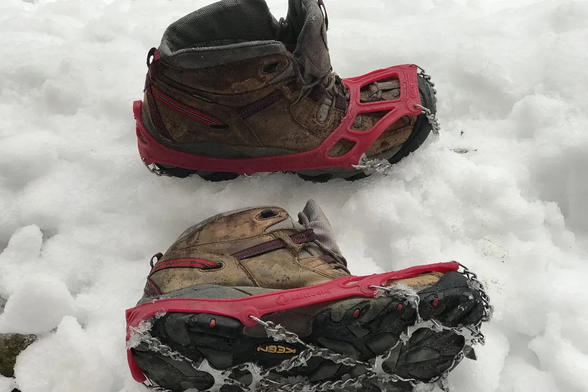Hiking boots fitted with red microspikes standing in snow