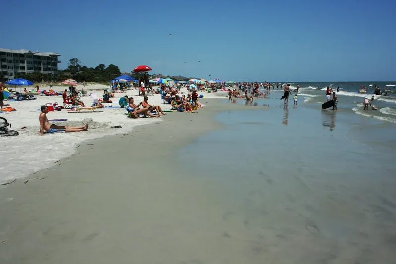 A wide, flat beach on Hilton Head Island with firm sand, gentle surf and a few people walking