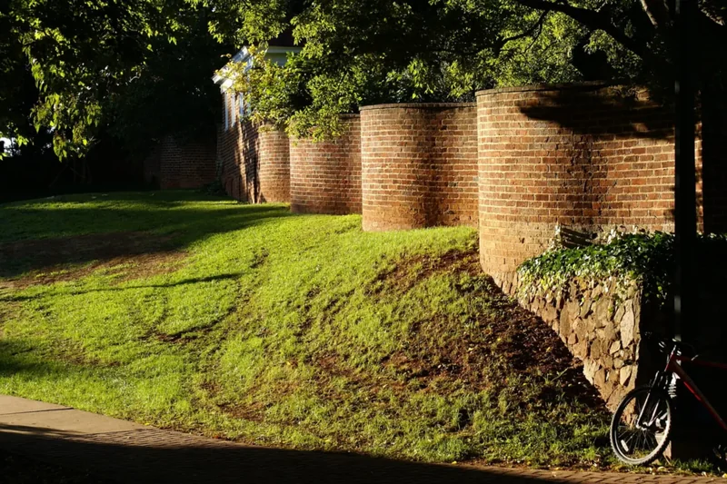 Curving brick serpentine walls beside a sloping lawn at the University of Virginia, a bicycle leaning on the wall