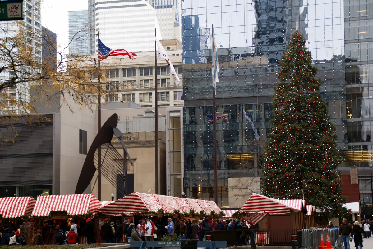 Christkindlmarket huts with red and white awnings in Daley Plaza, with the rust-brown Daley Center behind