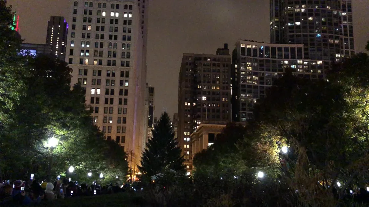 The City of Chicago Christmas Tree lit at night in Millennium Park, with crowds and skyscrapers around it