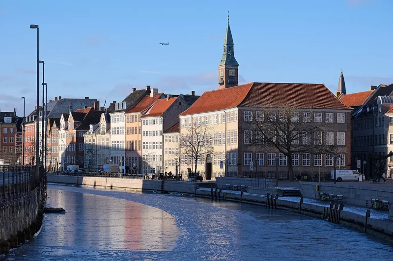 Ice on the canal at Gammel Strand in Copenhagen, with gabled townhouses and a church spire in low winter sun