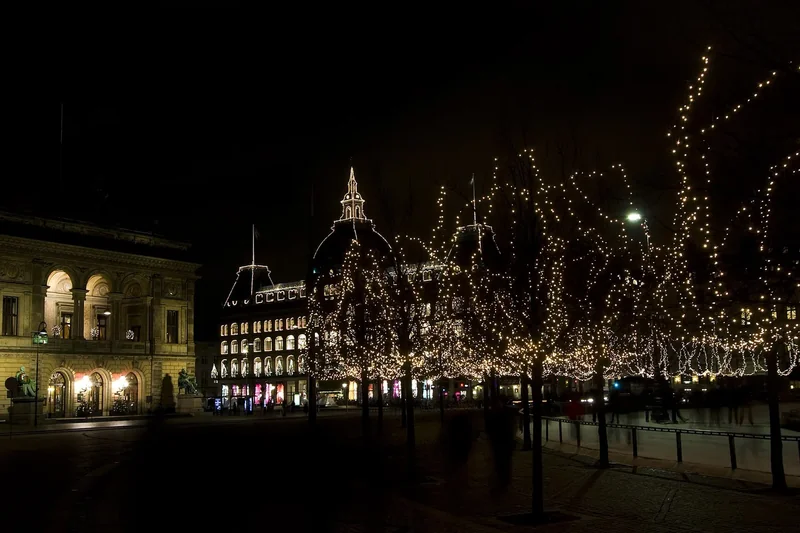 Kongens Nytorv at night in December, bare trees strung with white lights and the lit facade of the Royal Danish Theatre