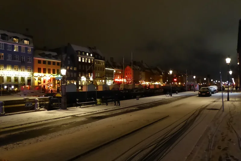 Snow on the quay at Nyhavn at night, with lit gabled houses along the canal and street lamps