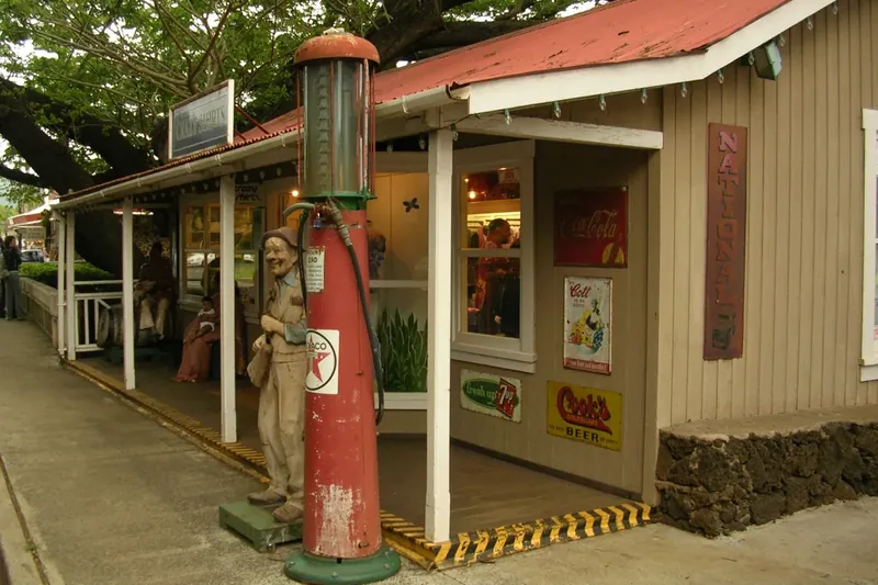 A plantation-era storefront with an old gas pump under a big tree in Kōloa