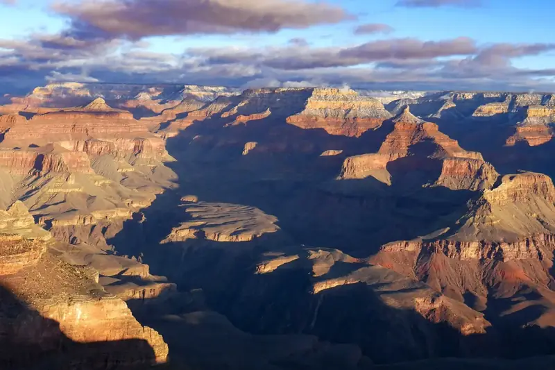 Golden sunrise light on buttes seen from Yavapai Point, with deep blue shadow below