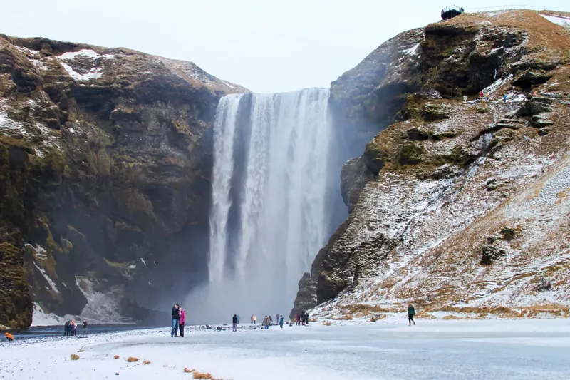 Skógafoss pouring over a cliff above snow-covered ground in winter