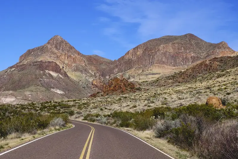 The paved Ross Maxwell Scenic Drive curving through desert scrub toward a flat-topped mountain