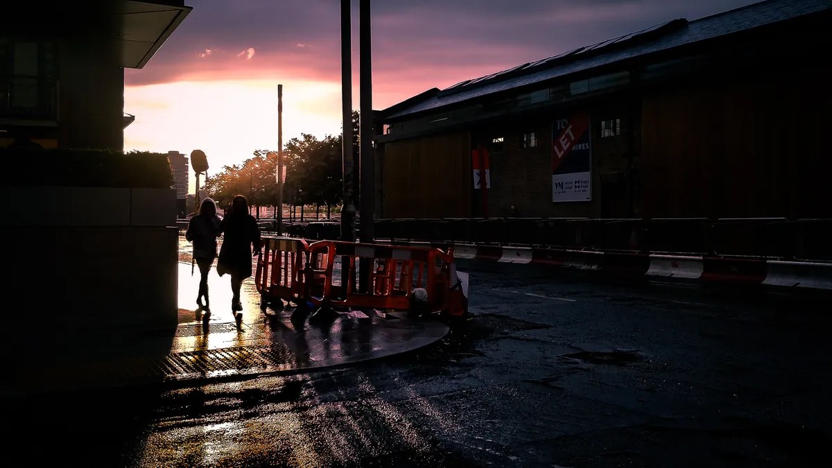 Two people walking along a rain-soaked Dublin street at sunset