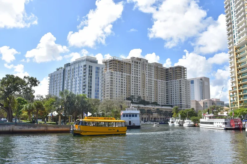 A yellow Water Taxi boat on the New River in Fort Lauderdale with high-rises behind
