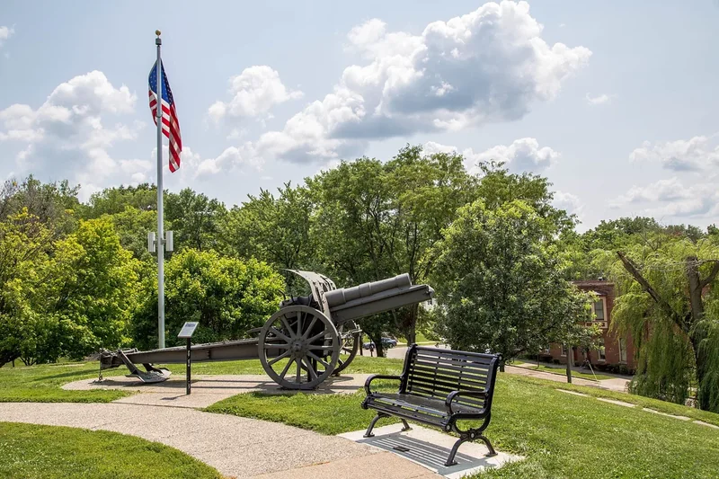 A cannon, a flagpole and a bench among trees and flowers in Grant Park, Galena