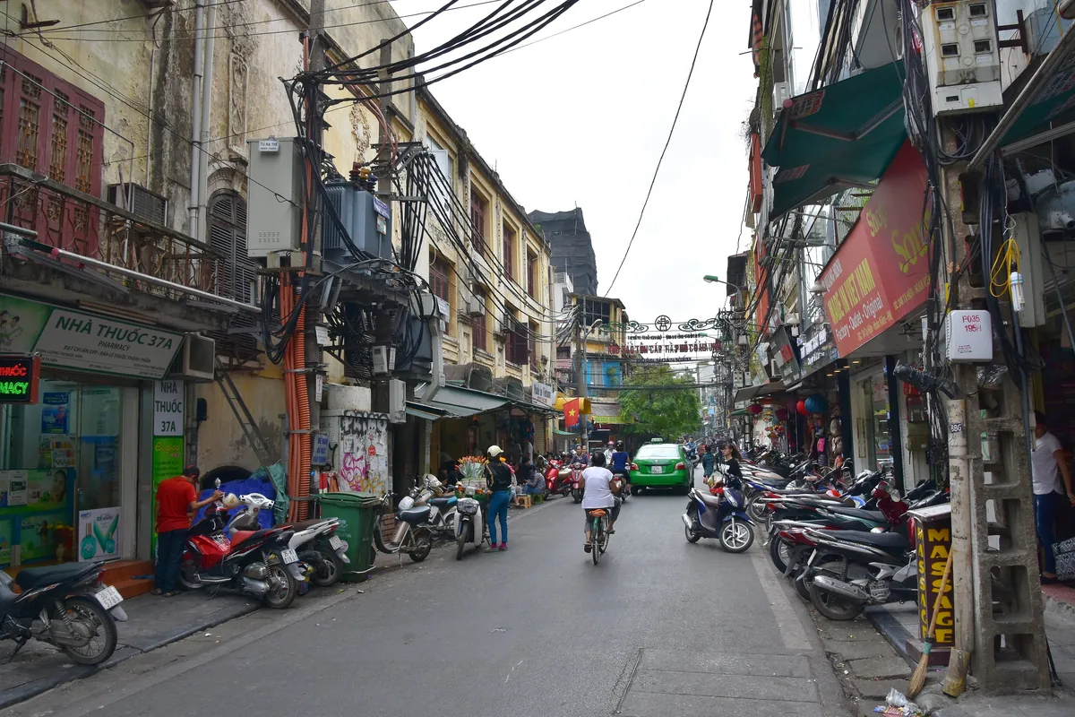 A busy Old Quarter street in Hanoi with shopfronts, signs and motorbikes