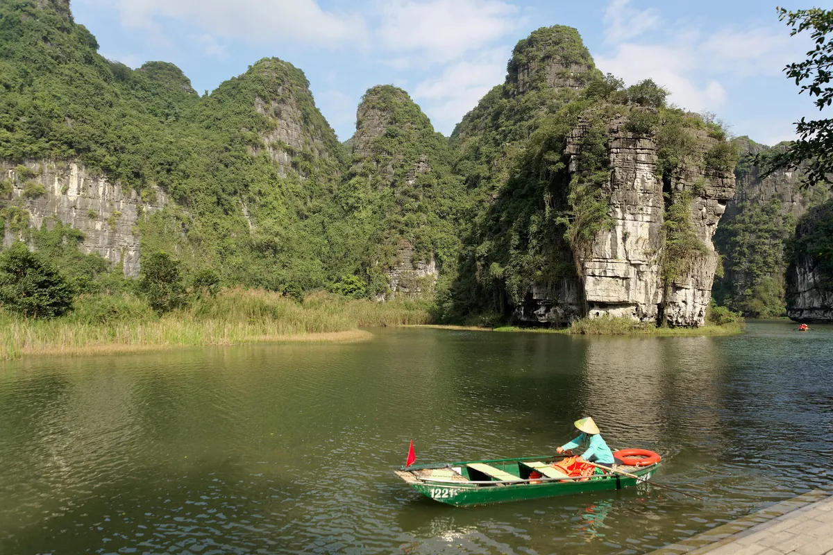 Limestone karst towers above the river at Trang An with a small boat on the water