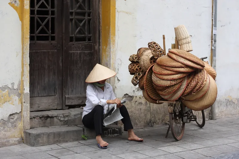 A street vendor in a conical hat with a loaded bicycle in Hanoi’s Old Quarter