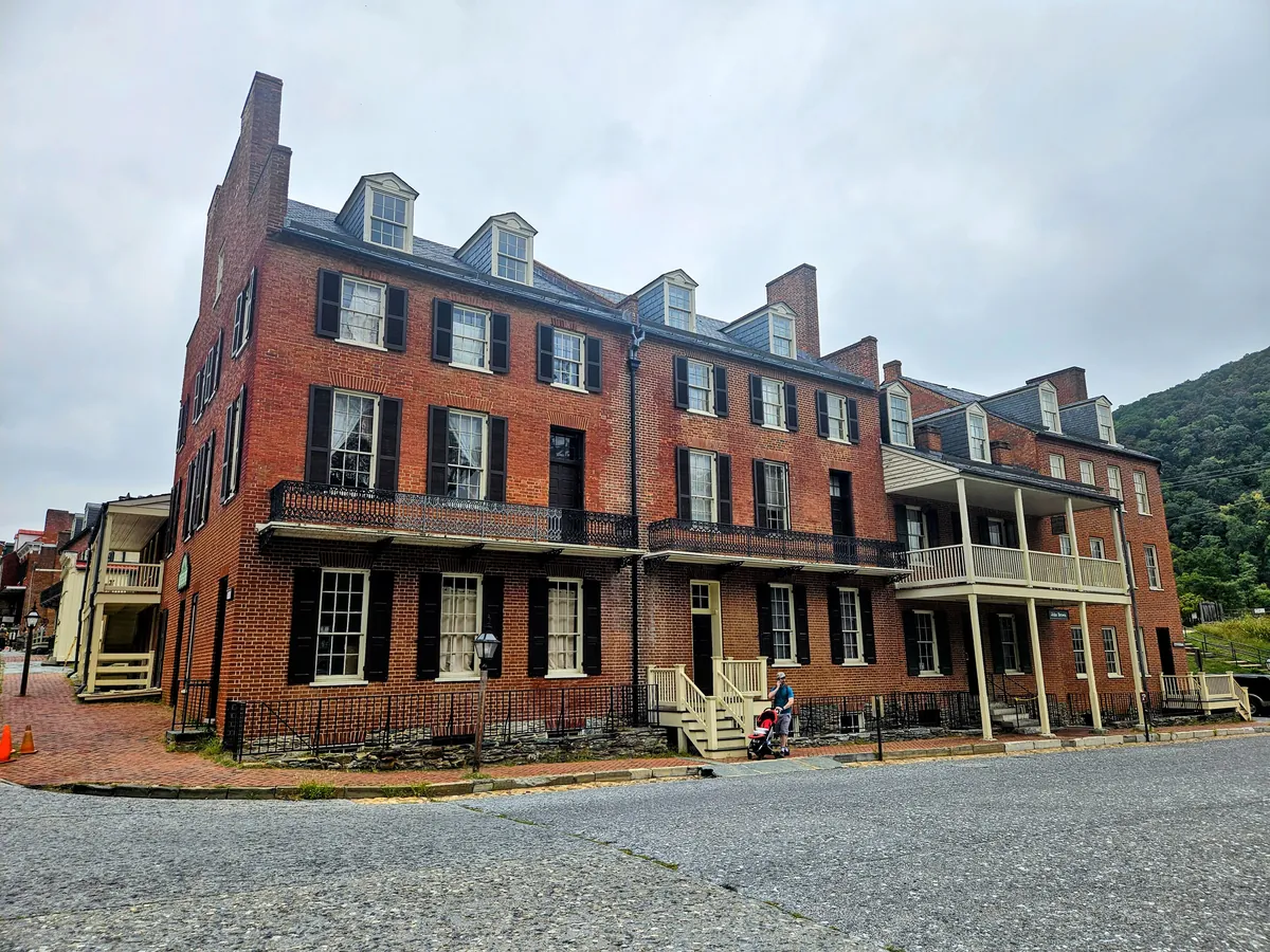 A long red-brick building with porches on a Lower Town street in Harpers Ferry under a cloudy sky
