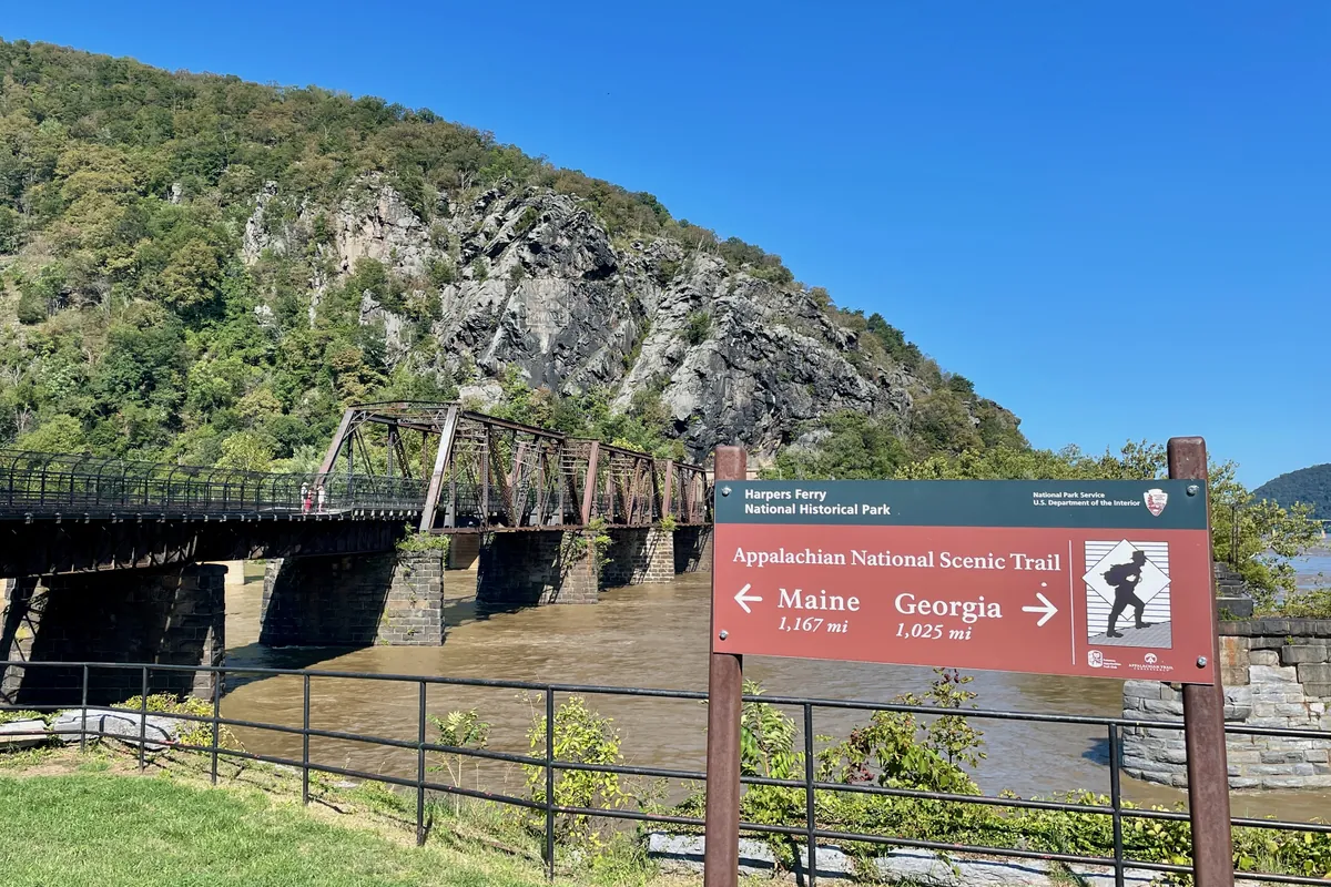 An Appalachian Trail sign beside the railroad bridge over the Potomac at Harpers Ferry, with Maryland Heights behind