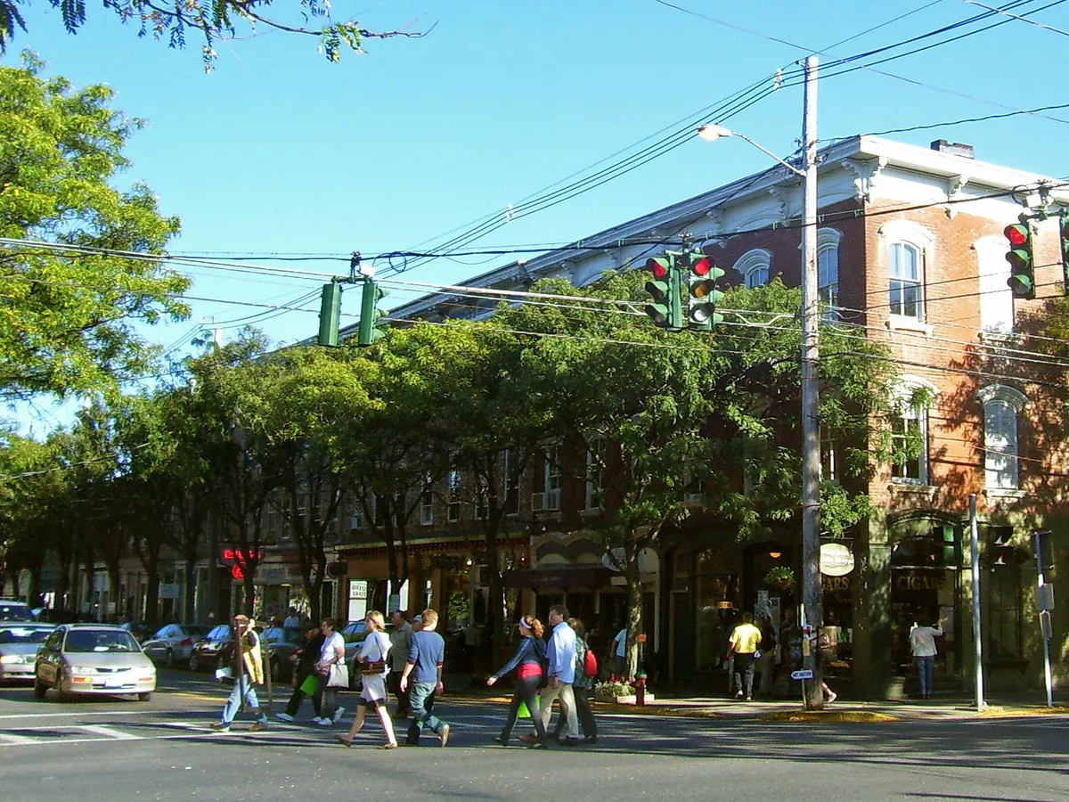 The main crossroads of Rhinebeck village with brick buildings, trees and people crossing the street