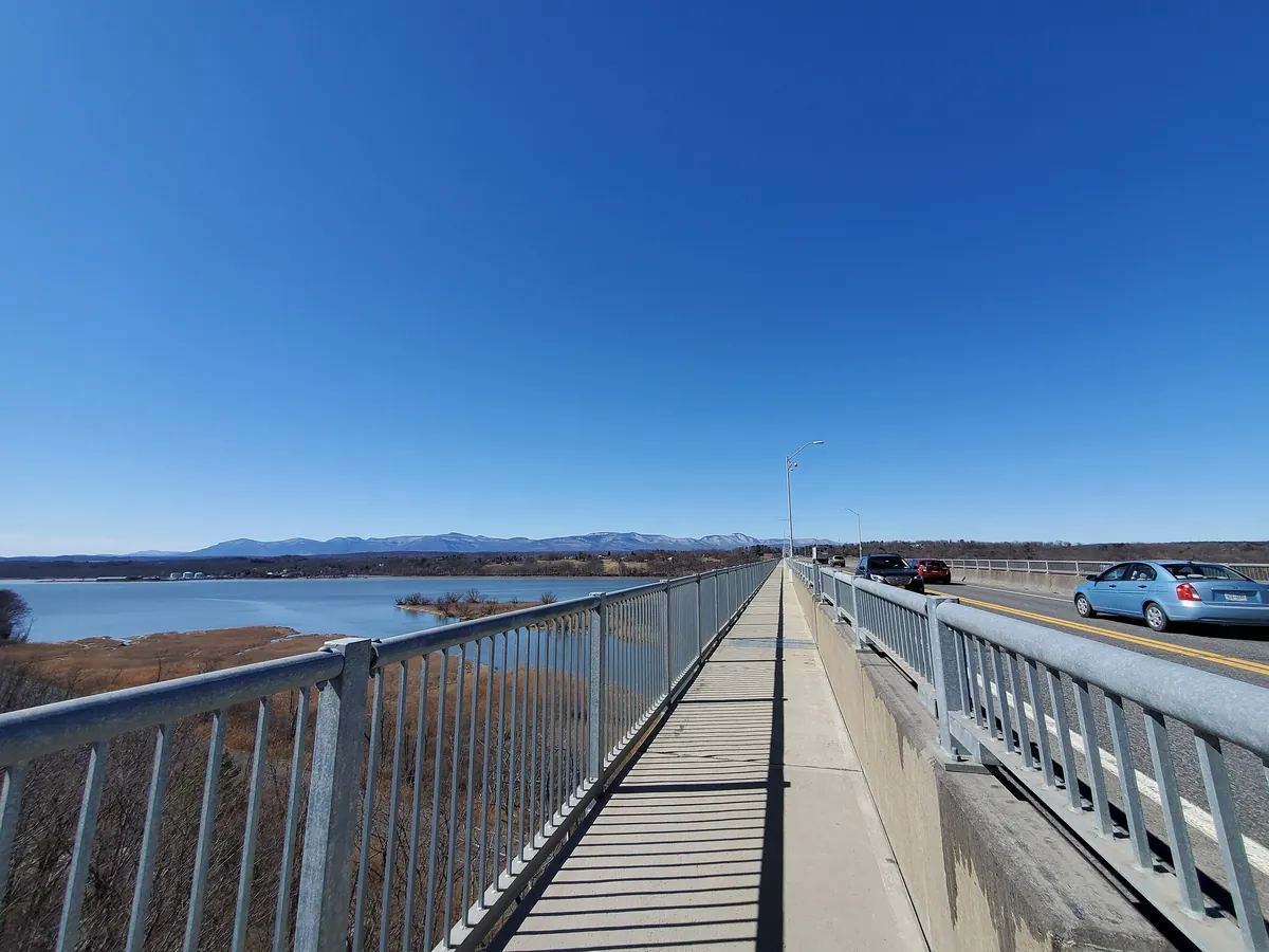 The fenced pedestrian walkway on the Rip Van Winkle Bridge running west toward the Catskills under a clear sky