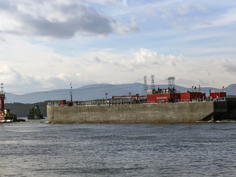 A tug pushing a barge on the Hudson River off Hudson in the evening, with the Catskills behind