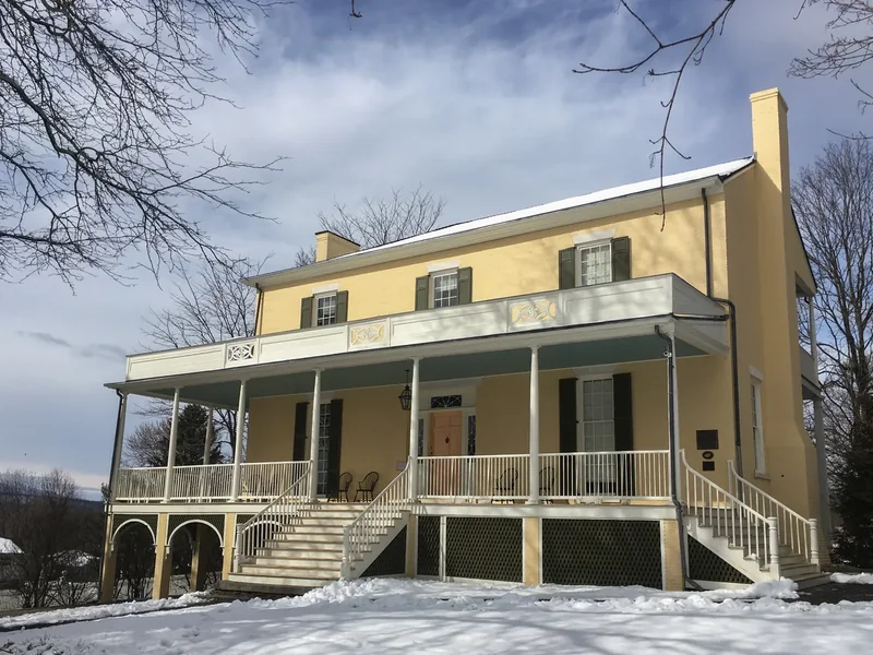 Thomas Cole’s yellow house at Cedar Grove in Catskill with a long porch, in winter with snow on the ground