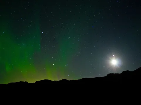 Green aurora bands across a starry sky above a dark Icelandic horizon