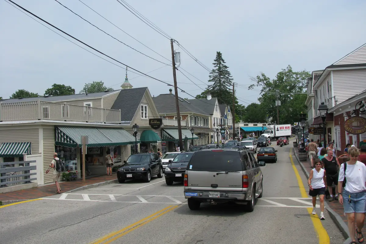 Shops with awnings and clapboard fronts along the street in Dock Square, Kennebunkport, with cars and people walking
