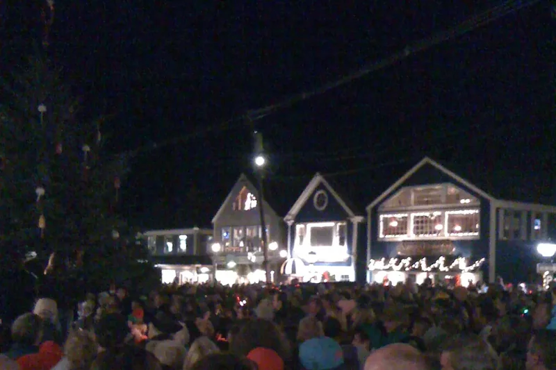 A crowd gathered at night in Kennebunkport during Christmas Prelude, with lit houses beyond