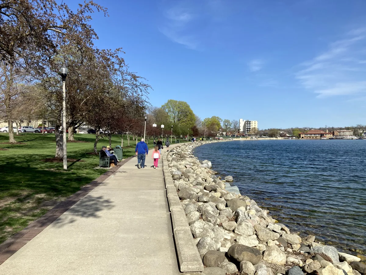 The Geneva Lake Shore Path, a paved walkway beside a rocky shoreline and blue water in spring