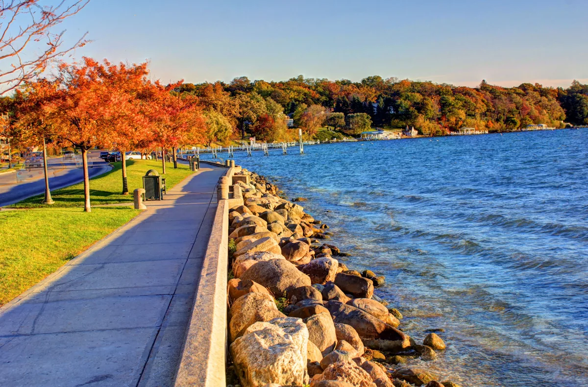 The Geneva Lake shoreline with a paved path, rocks and autumn trees